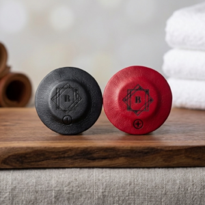 Pareja de imanes de neodimio bipolares forrados en piel premium roja y negra con logo grabado de BiomagArt sobre base de madera.