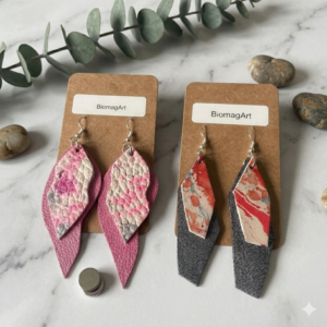 Set de dos pares de pendientes de cuero artesanos BiomagArt, diseños geométricos y orgánicos en rosa, negro metalizado y marmoleado, con imanes de neodimio ocultos sobre fondo de mármol.